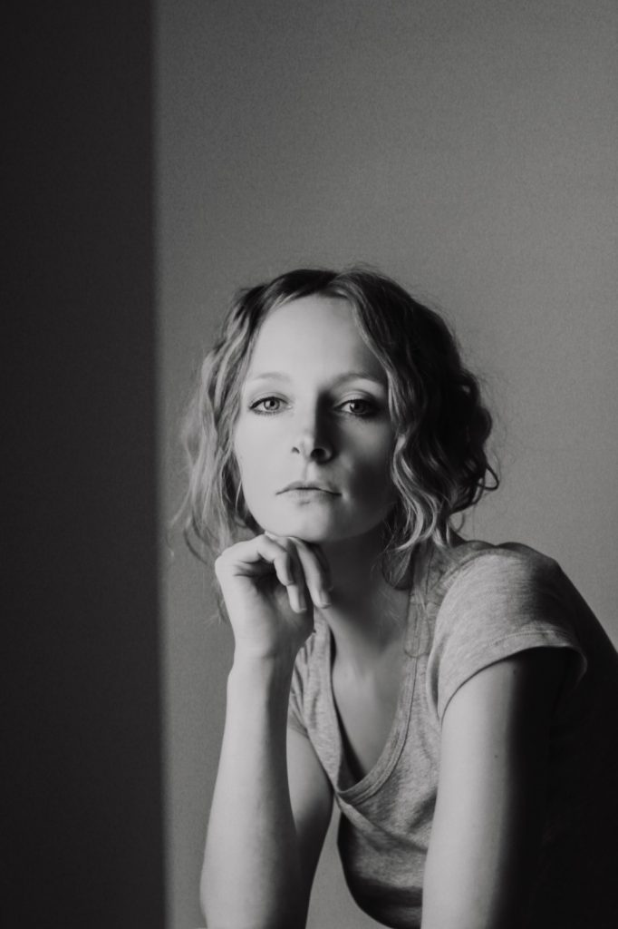 Frau mit Locken und grauem T-Shirt stützt Kopf auf die Hand